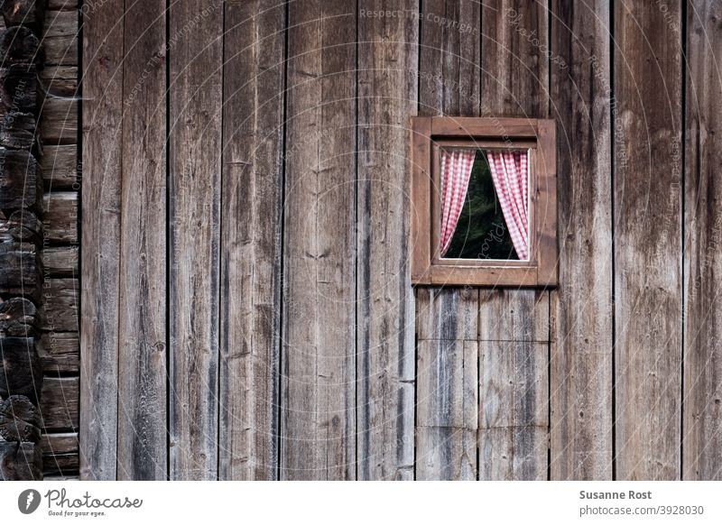 A house wall made of wide wooden beams with a small wooden window with red and white checked curtains at Window Facade Wooden window Wooden facade Old