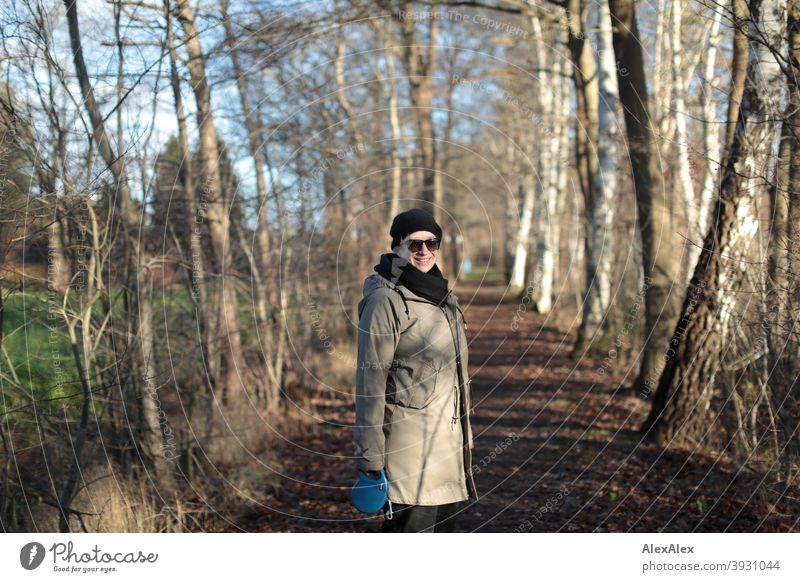 Young woman with sunglasses stands on a path surrounded by trees in autumn and turns around smiling Woman Autumn Winter off Bushes out portrait Sunglasses