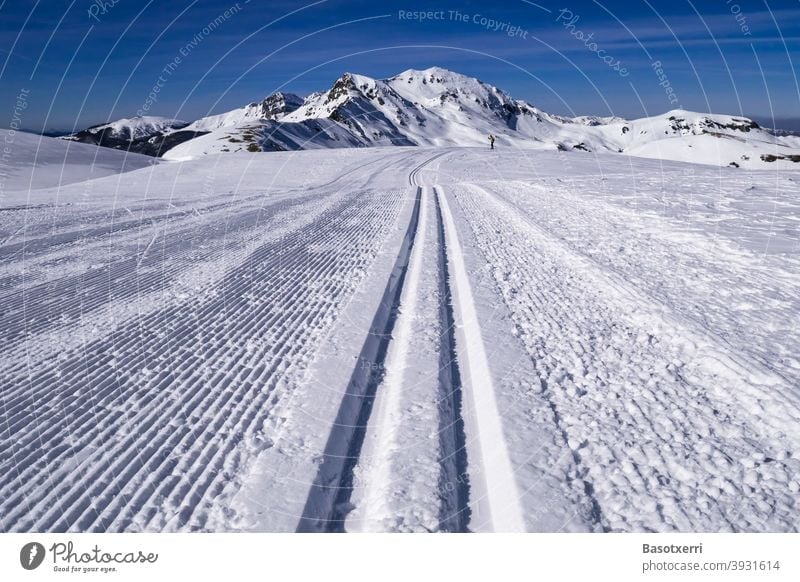 Traced cross-country skiing track in the mountains. Small person (cross-country skier) in the background. Isaba/Belagua, Navarra in the Spanish Pyrenees.