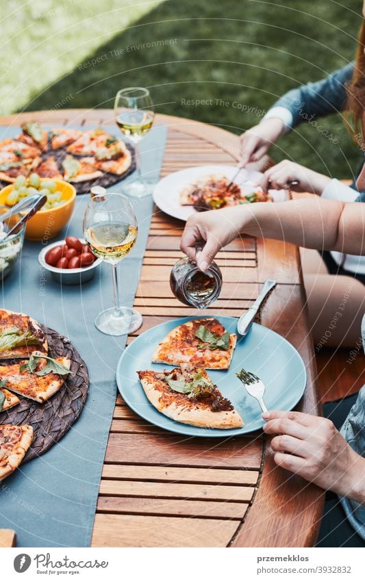 Family and friends having meal - pizza, salads, fruits and drinking white wine during summer picnic outdoor dinner in a home garden backyard beverage