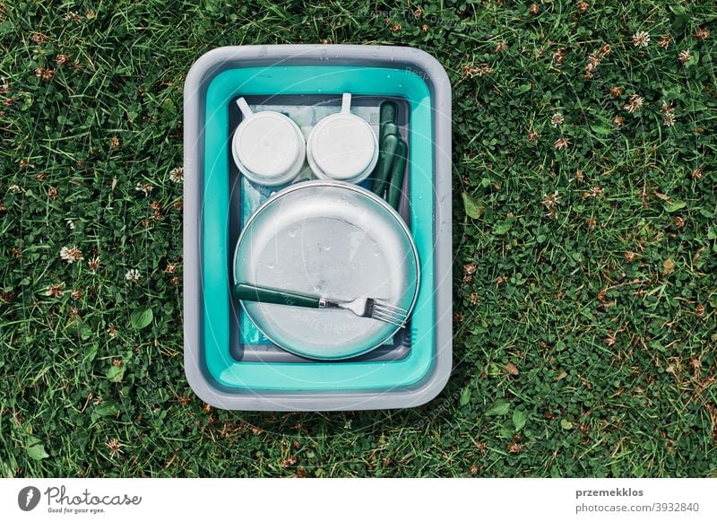 Washing up bowl filled with the washed outdoor dishes, plates, cups and cutlery put on grass camp camping campsite cleaning cleanup dish wash dish washing life