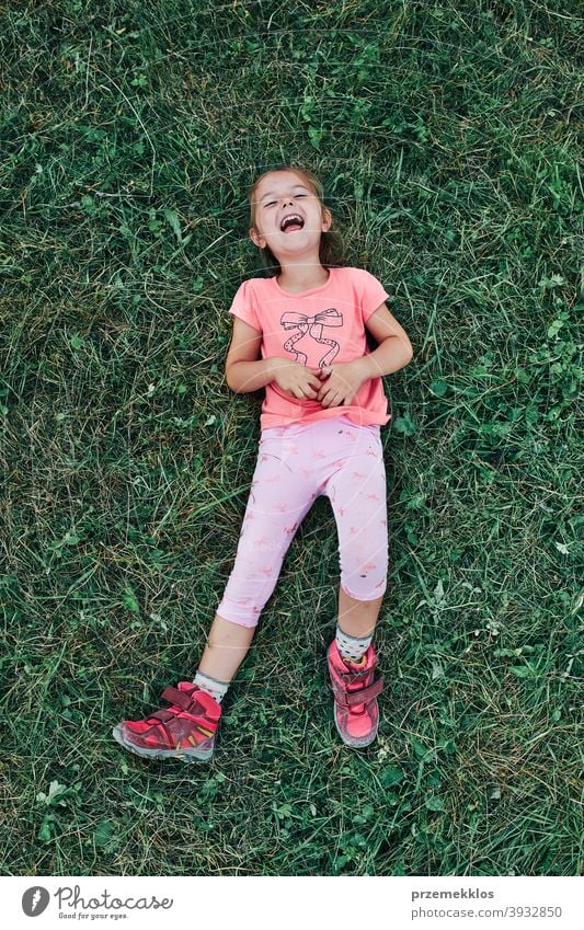 Little girl laying playing on grass enjoying summer day during vacation trip happy excitement enjoyment leisure emotion positive lying lifestyle activity