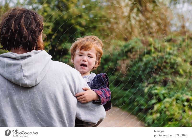 Unhappy crying toddler being carried off by his father away baby boy carried away carrying casual caucasian cute danger dangerous ginger green background
