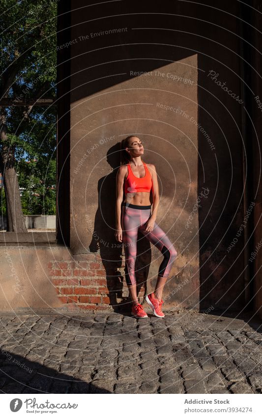 Slim sportswoman standing near building on street fit slim athlete runner city activewear summer female wall shabby wellbeing lean wellness fitness training