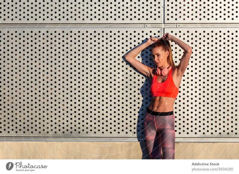 Sportswoman standing near building on street sportswoman runner city athlete slim fit summer sunny female sportswear wall workout relax urban rest positive
