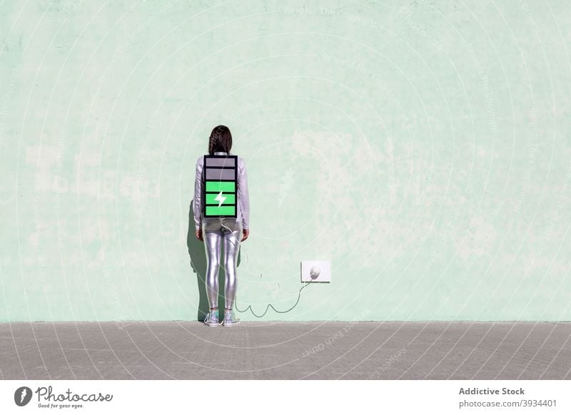 Anonymous woman with creative big battery backpack indicating charging process charge load energy digital concept connection street wall shadow female young