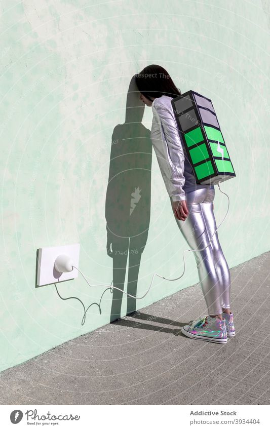 Anonymous tired woman charging big battery backpack on street exhausted recharge load energy connection creative concept wall shadow female young style trendy