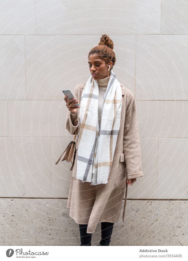Stylish young ethnic woman messaging on smartphone while walking on street using entrepreneur work message laptop city browsing online female african american