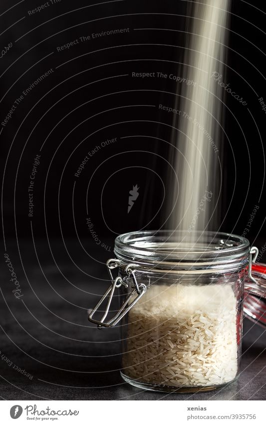 Into a storage jar with rice against a dark background pours a bright beam of rice from above Rice Supply Glassware Nutrition Food Storage plastic-free