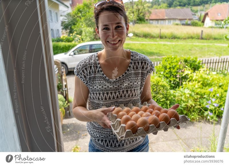 Delivery of fresh eggs at the house door by a young smiling woman. indoors delivery home season service cargo work cardboard customer retail pay sales logistics