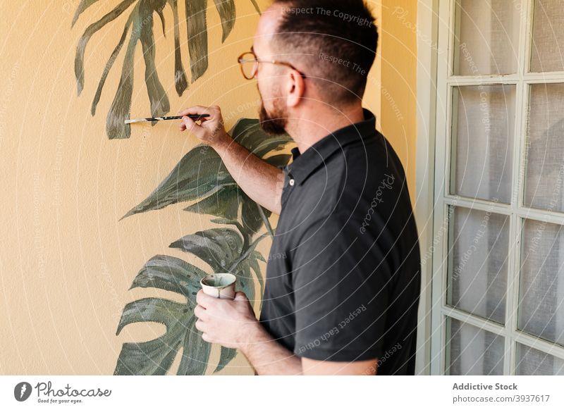 Male artist painting on wall at home painter leaf man interior apartment decorate monstera male green creative style contemporary modern flat plant design
