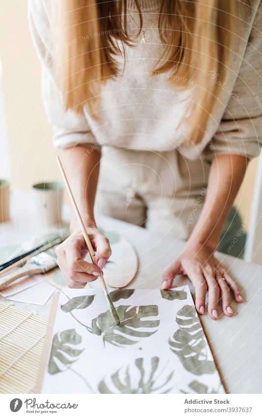 Crop painter creating picture of monstera leaves on paper artist woman leaf plant workshop paintbrush female table painting green creative talent craft sheet