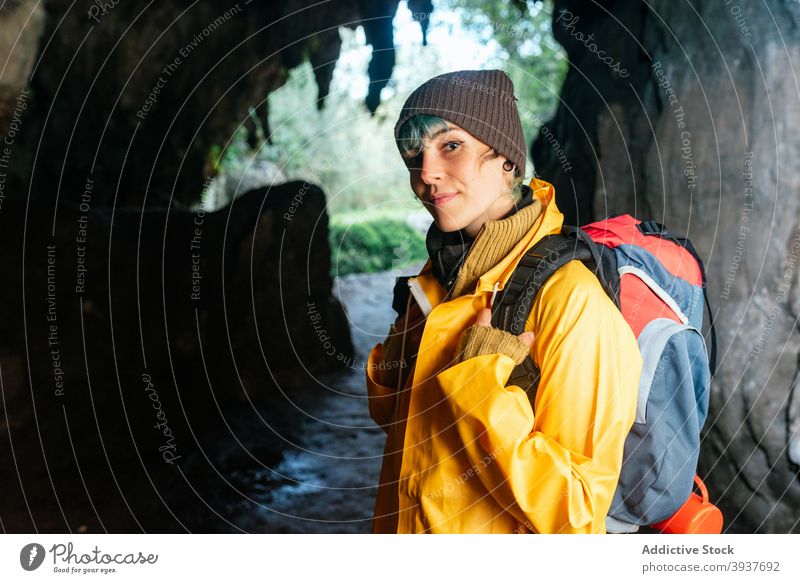 Delighted female explorer with backpack looking at camera traveler woman cheerful passage arch rocky outerwear autumn vacation cobijero beach asturias spain