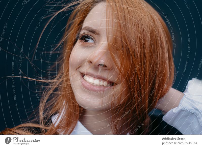 Smiling woman with wind in hair on street redhead flying hair carefree charming red hair enjoy smile female content young ginger cheerful city style positive