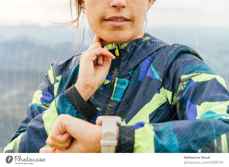 Sporty young ethnic woman checking wristwatch on mountain top during hiking sportswoman time training hike activity sporty energy workout female activewear