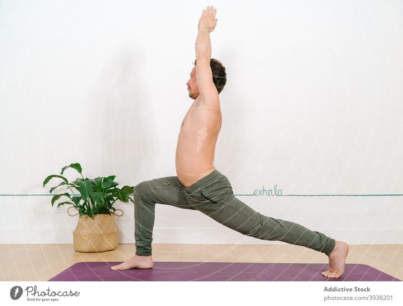 Man standing in Crescent Lunge pose in yoga studio man practice crescent lunge pose anjaneyasana mindfulness harmony peaceful naked torso male zen tranquil