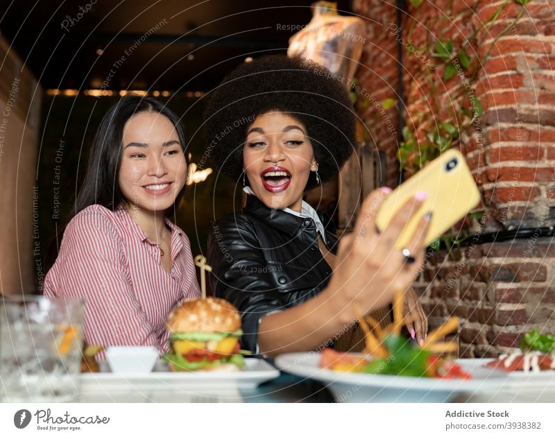 Multiracial girlfriends taking selfie during dinner in restaurant smartphone together cheerful funny grimace food young women multiethnic multiracial diverse