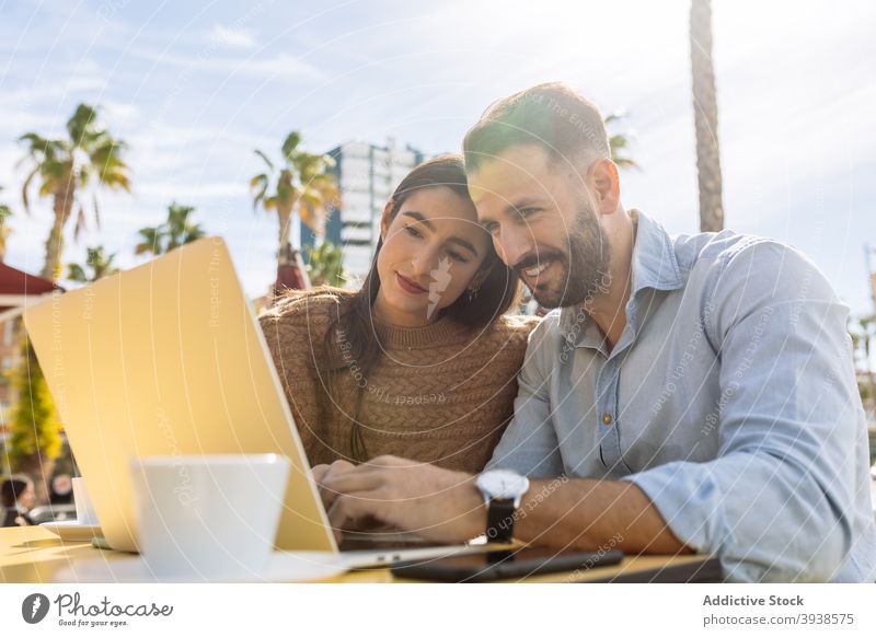 Cheerful young couple sharing laptop and laughing in street cafe watch video having fun love together cheerful date point excited funny boyfriend girlfriend