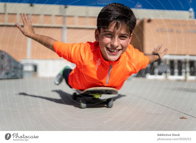Happy ethnic male teenager lying on skateboard and smiling boy ride balance fun activity hobby cheerful dynamic square optimist joy young dark hair casual happy