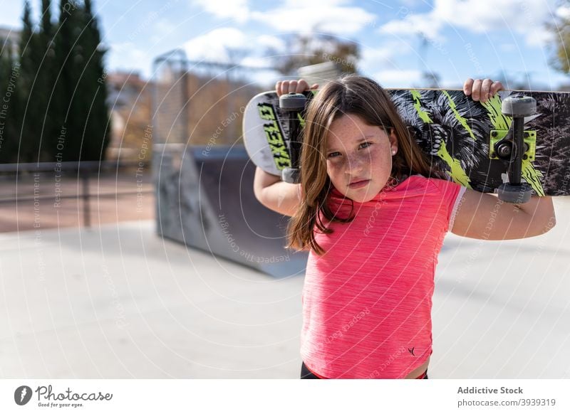 Cute girl standing near ramp with skateboard after riding skate park rest serious training active hobby relax childhood kid long hair pensive adorable casual