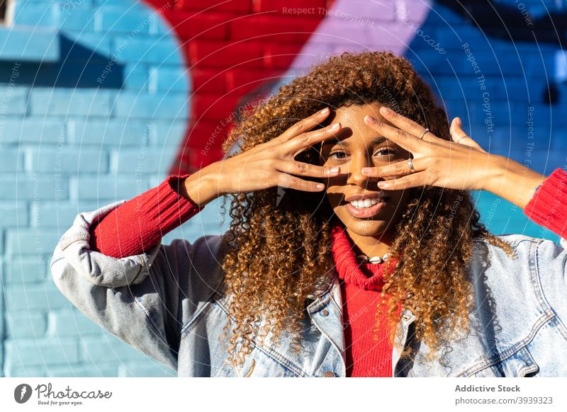 Joyful young black gesturing and smiling near wall with graffiti woman touch face smile happy street subculture gesture style positive street art trendy female
