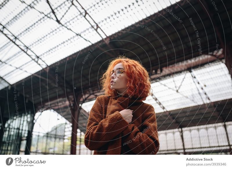 Young redhead woman in coat standing at railroad station red hair railway style trendy building female wavy hair hairstyle appearance urban city modern