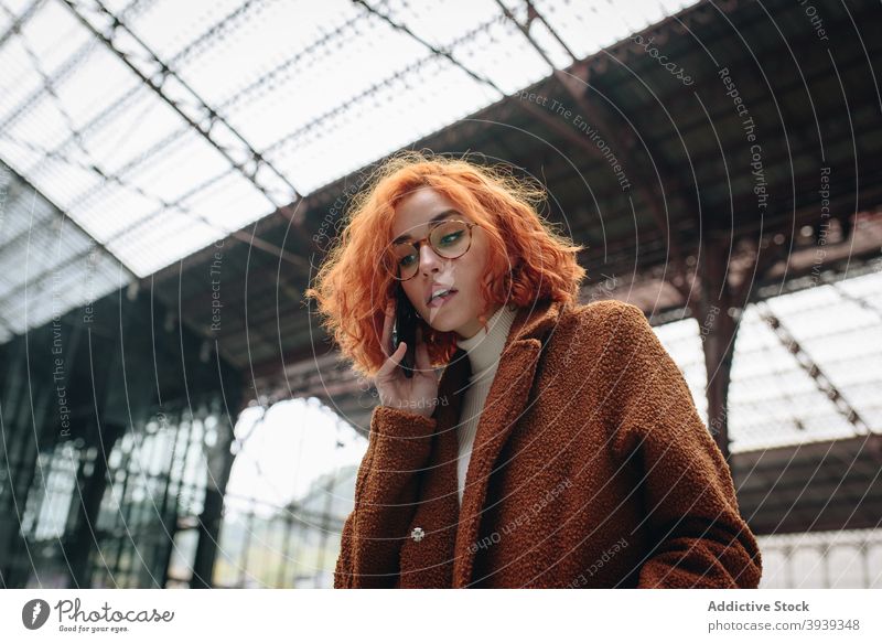 Cheerful woman talking on smartphone at railway station cheerful speak railroad redhead red hair female mobile conversation phone call communicate smile chat