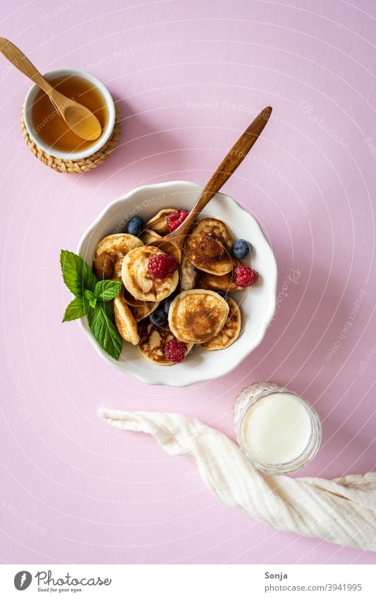 Breakfast of mini pancakes and fresh berries in a bowl on a pink background. Miniature Berries Fresh Delicious Milk Honey plan cute Food Nutrition Red