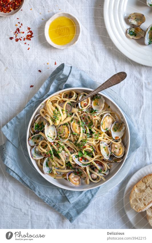 Top down view of pasta vongole, linguini with clams red pepper flakes and olive oil on white background with blue napkin food styling food photography