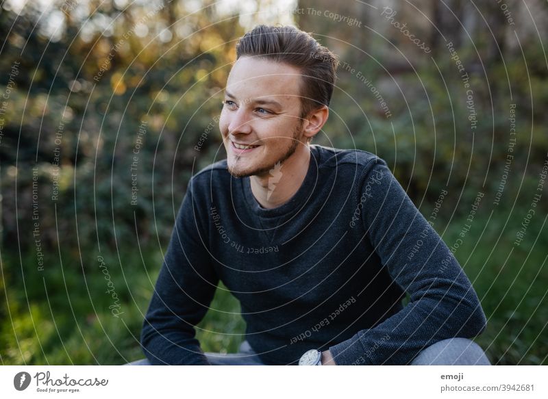 young man smiling outside Outdoors Green masculine more adult Upper body arms folded Profile Young man Man Friendliness Smiling Positive Impish Congenial