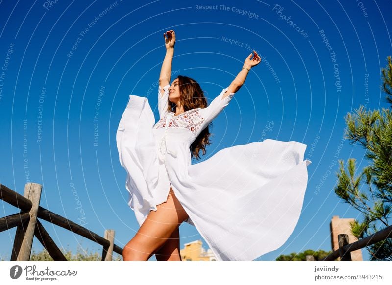 Young woman raising her arms in a beautiful white dress against a blue sky fashion girl wave open hair female copyspace extensions hairstyle fashionable model