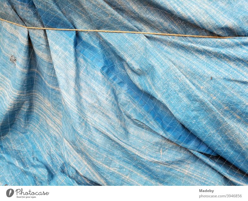Verwaschene blaue Plane aus Kunststoff gut verschnürt als Schutz vor Regen und Sturm Schutzplane Blau denim Seil Regenschutz Plastik Hintergrund Fläche Falten