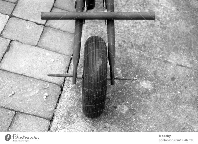 Front wheel of a self-made tricycle made of parts of an old wheelbarrow on grey paving stones and grey concrete in classic black and white Tricycle