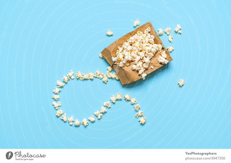 Popcorn in a paper bag isolated on blue background. Popcorn bag exploding, top view abundance appetizer buttery colored background comfort food concept crunchy