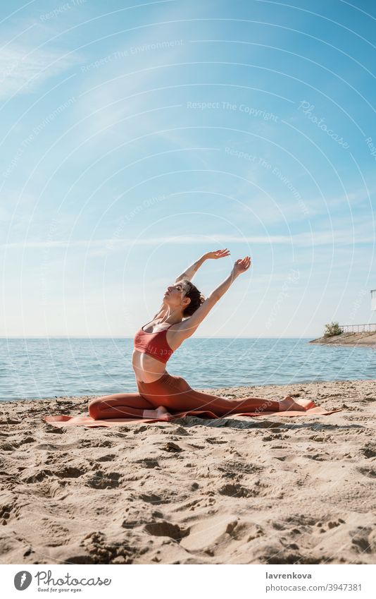 Young female in orange top and leggins practising Pigeon pose on a beach in the morning yogini pretty mat mind nature practicing hamstring sea Hip opener