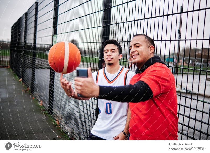 Friends taking a selfie by the fence of a basketball court outdoors. player horizontal teenage vitality aspirations basketball player male concentrated