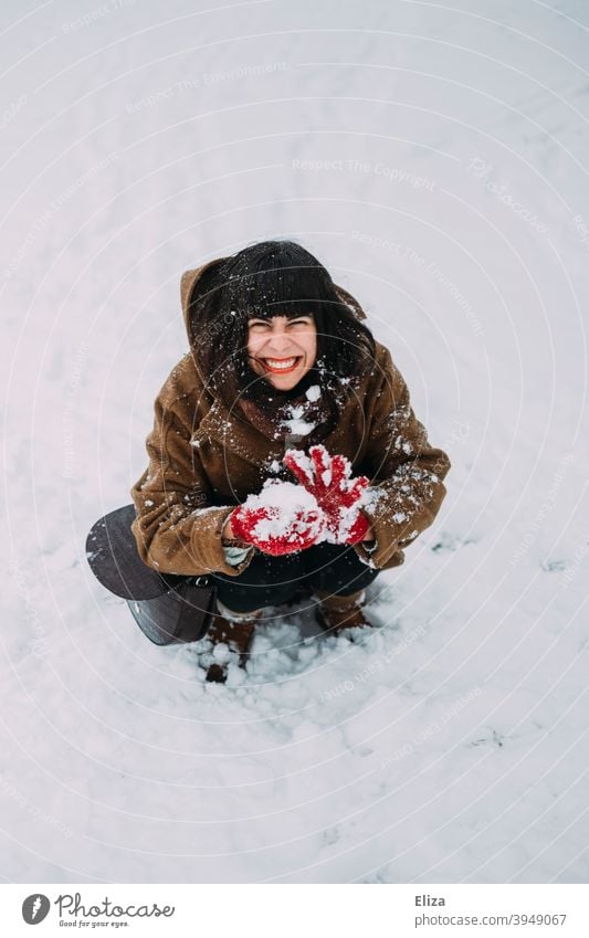 A woman sits in the snow, forms a snowball and grins cheekily Woman Snow Snowball Impish mischievous Laughter Grinning Brash fun Winter Snowball fight Funny Joy