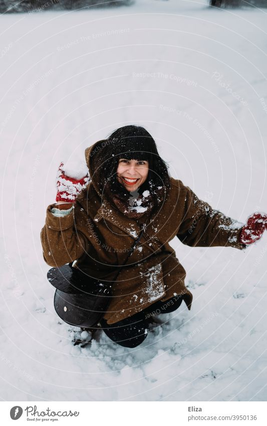 A young woman sits in the snow and throws a snowball Snowball Throw Woman youthful Brunette Winter Snowball fight fun Joy Smiling Sit White Human being