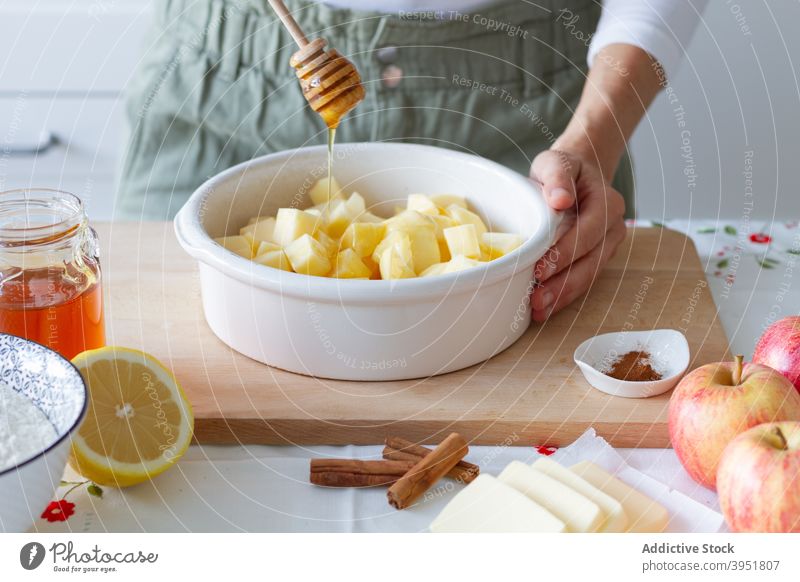 Crop person adding honey to apples cook crumble ingredient pastry kitchen home table fresh lemon flour cinnamon butter pie homemade recipe prepare pan food bake