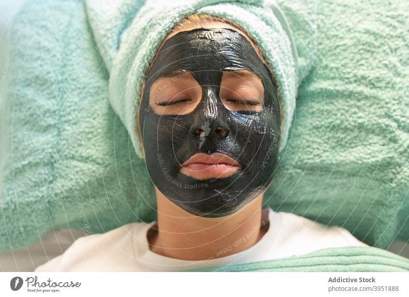 Young woman with black facial mask having in salon skin care clay procedure cosmetic astonish wow gesture joy playful female young casual towel cheerful client