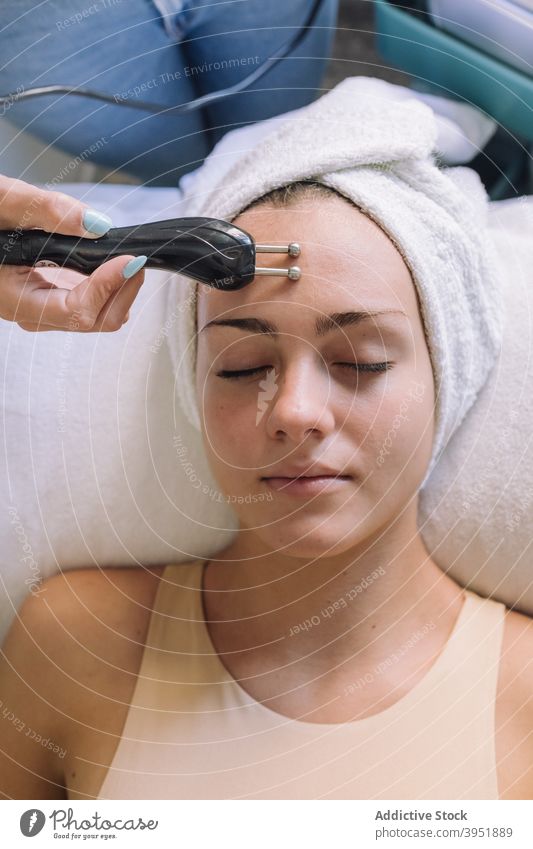 Relaxed young woman lying on couch with closed eyes during microcurrent facial treatment women skin care rejuvenate anti aging procedure cosmetician client spa