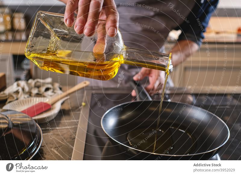 Unrecognizable man pouring oil into saucepan kitchen home add chef modern bottle male ingredient recipe middle age mature lunch dinner culinary cook glass beard
