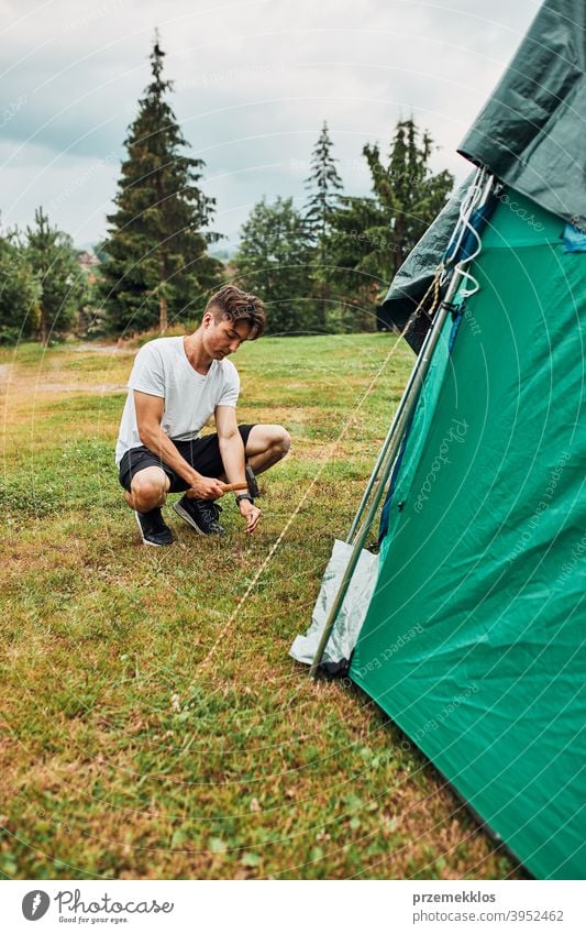 Young man putting up a tent on camping during summer vacation trip stake peg hammer grass setting pitching teenager young copy space leisure countryside person