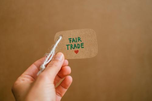Hand holding a label that says Fair Trade. Buy fair trade goods. fairly traded Shopping Label conscious consumption fairtrade Responsibility