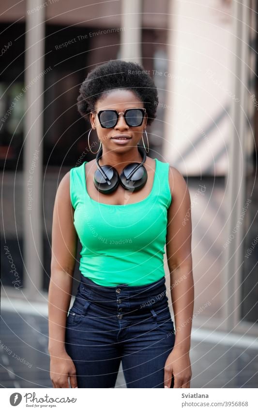 A young African woman wearing headphones and sunglasses smiles happily and looks at the camera african happy smiling positive looking girl music afro background