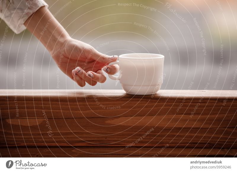 Morning coffee cup. Female hand holds white cup of morning hot drink - coffee or tea on the balcony on the background of mountain nature. female woman people