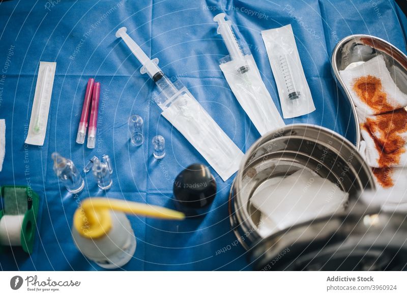 Operating room table with a blue tablecloth with needles, iodine gauze, anesthesia and a metal pot CrotoChic anesthetic break condition container cure diagnosis