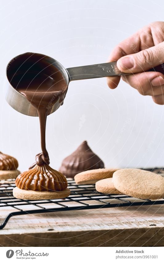 Crop cook adding chocolate topping on cookies pour prepare sweet dessert caramel cream table pastry culinary yummy homemade gastronomy food meal treat bakery