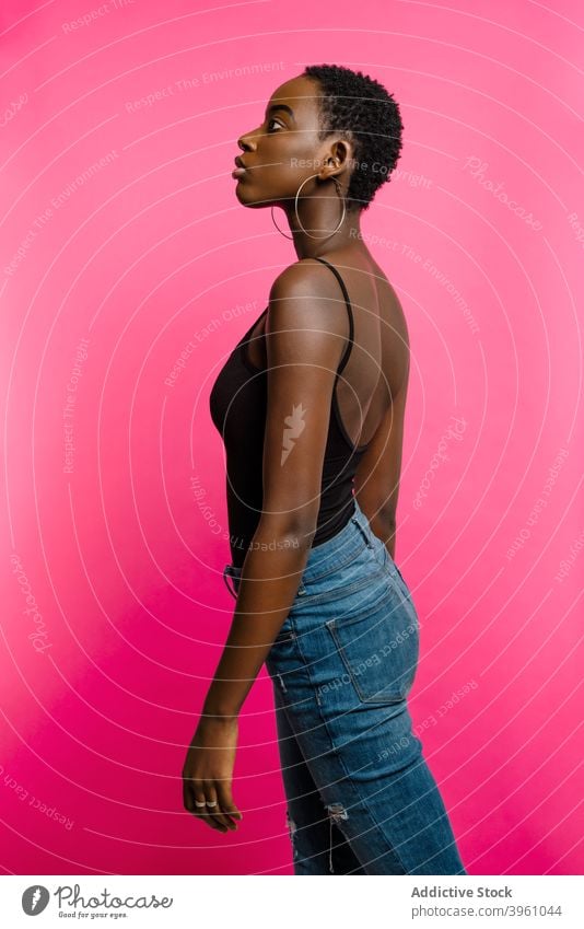 Young black woman standing in pink studio confident model portrait positive self assured fashion style female young african american ethnic fit top jeans trendy