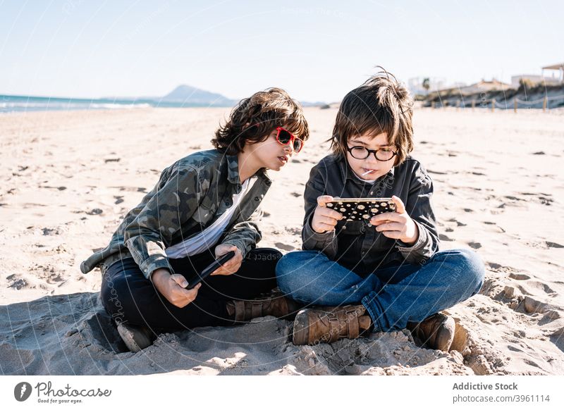 Two children playing with their mobile on the beach boy smartphone authentic active break coast concept fun holiday kid lifestyle nature outdoor outside people